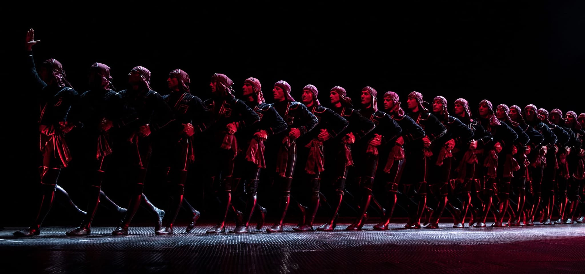 Sukhishvili dancers in formation on a darkened stage under red light